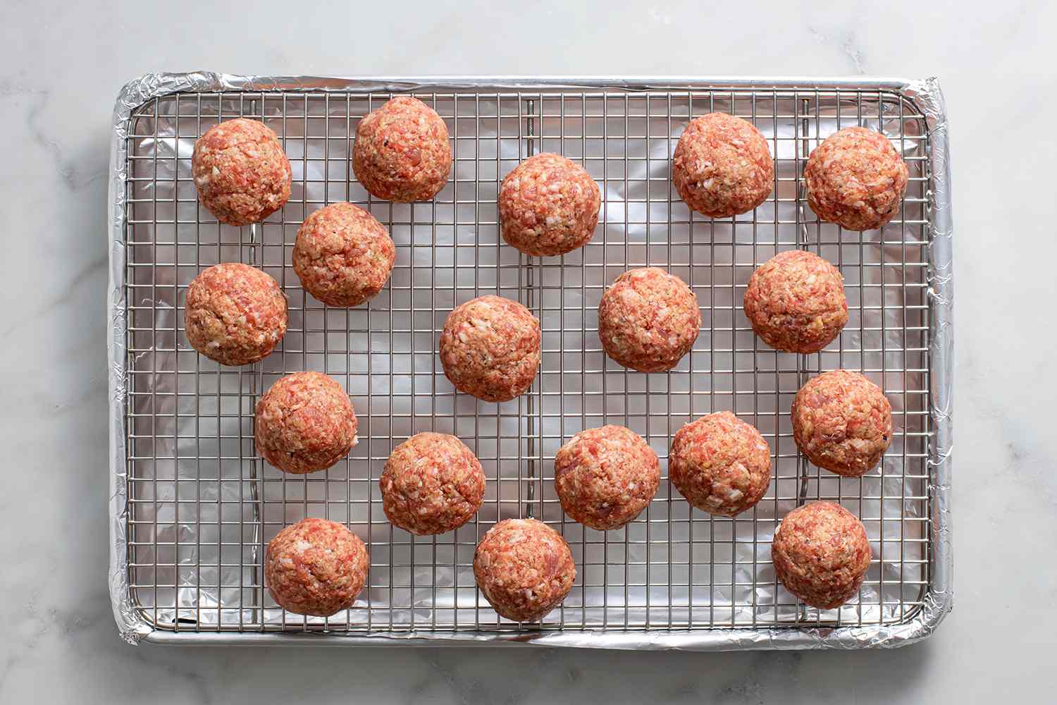 Raw meatballs on a rack over a baking sheet