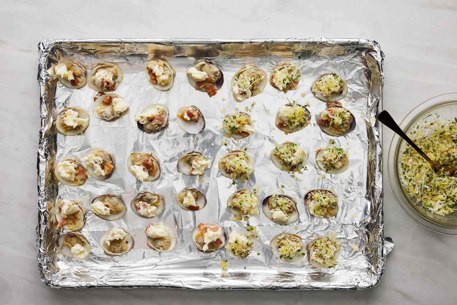 panko mixture placed on top of buttered opened clams on baking sheet