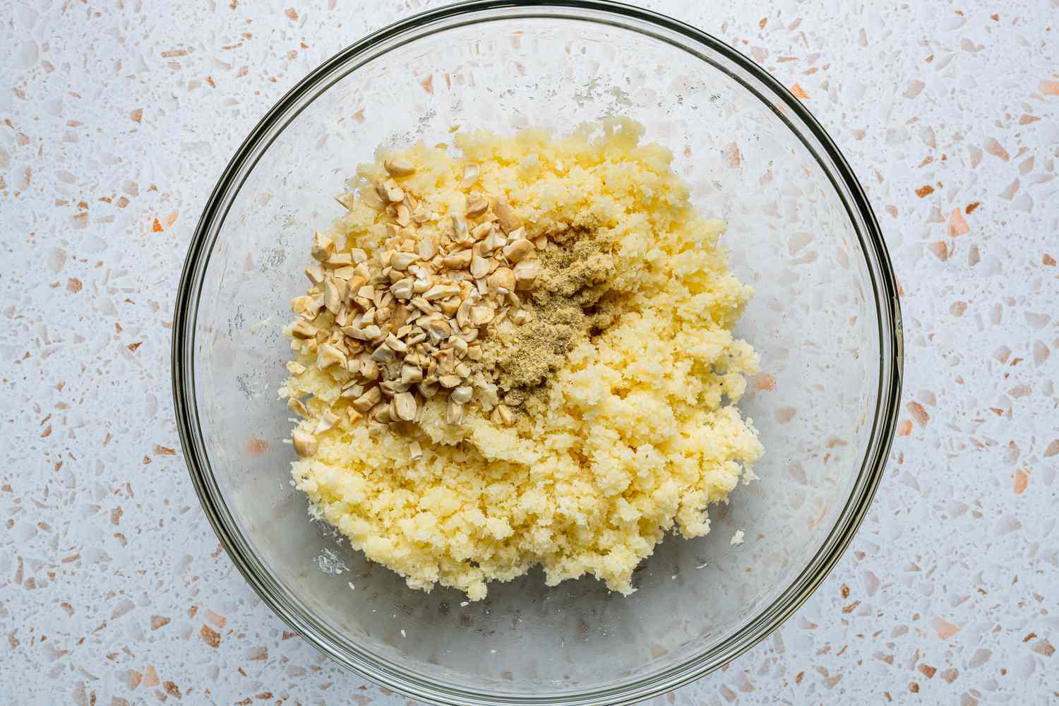 A large glass bowl of coconut-milk powder and syrup mixture with ground cardamom and broken cashews