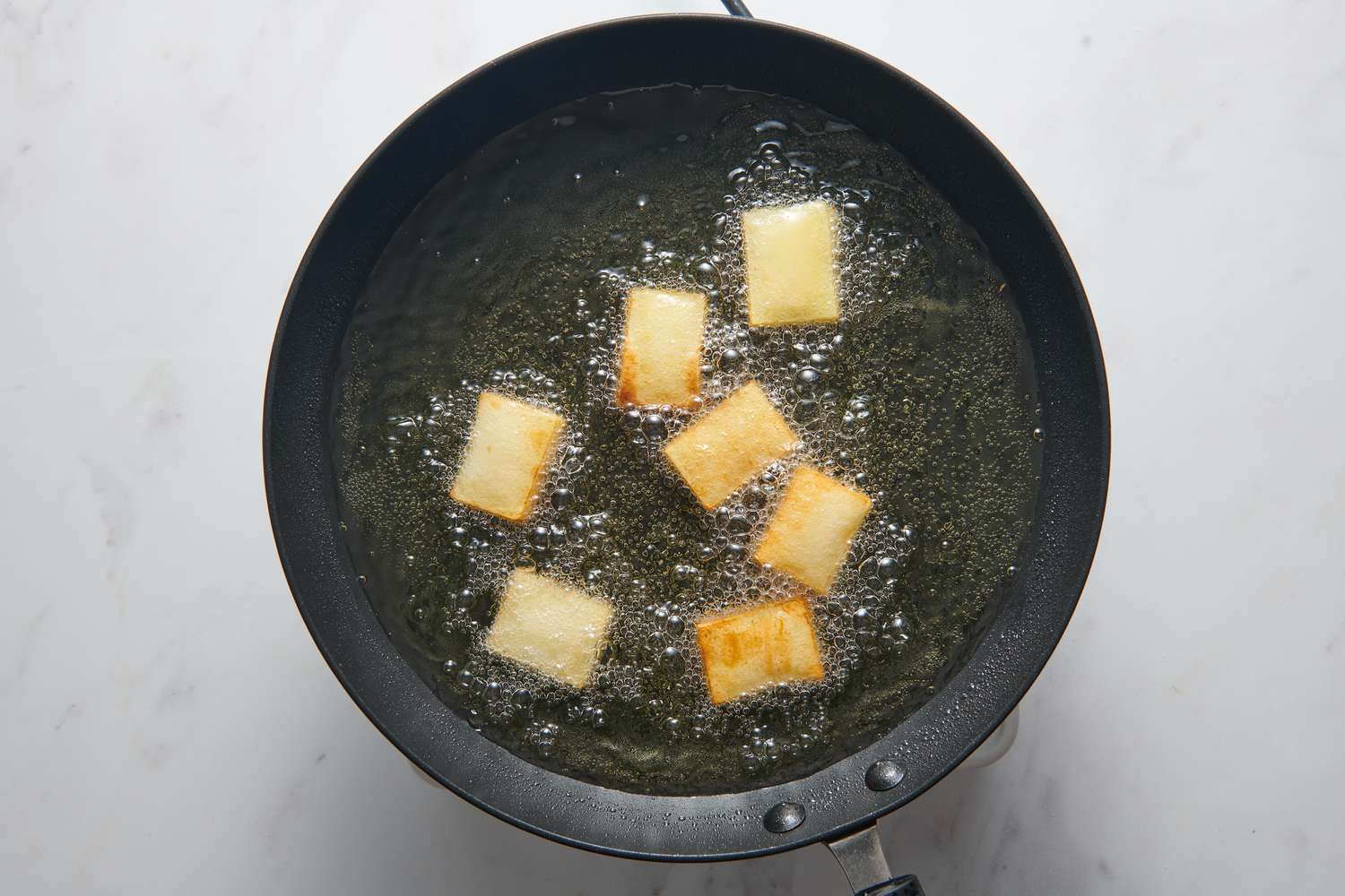 A pan with small rectangular stacks of thinly sliced potatoes frying in oil