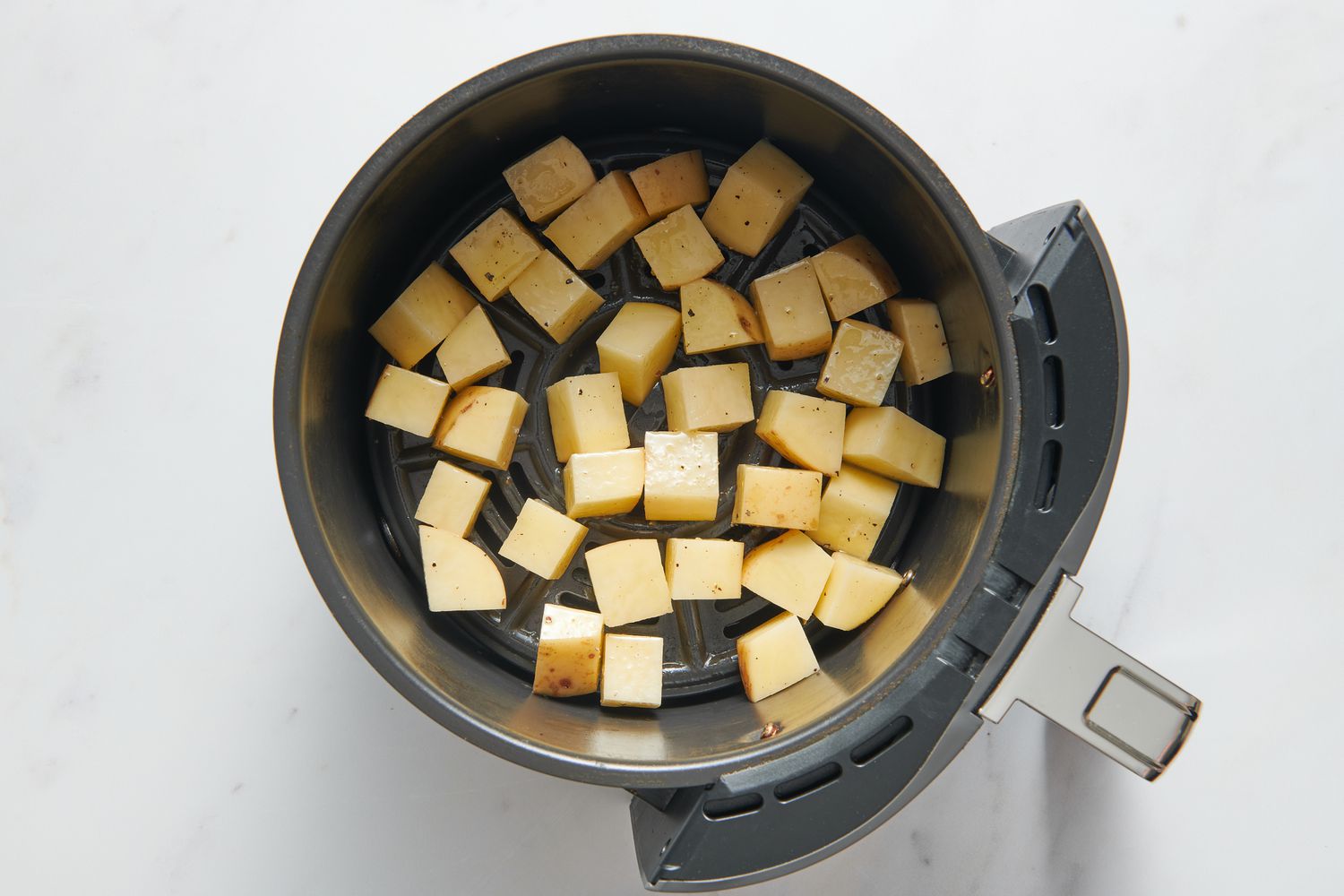 An air fryer basket with oil tossed russet potato cubes