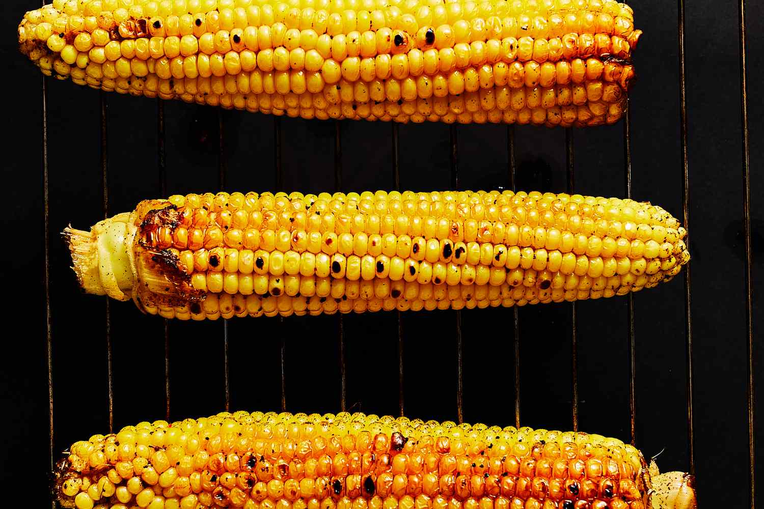 Slightly charred ears of corn cooking on on a grill