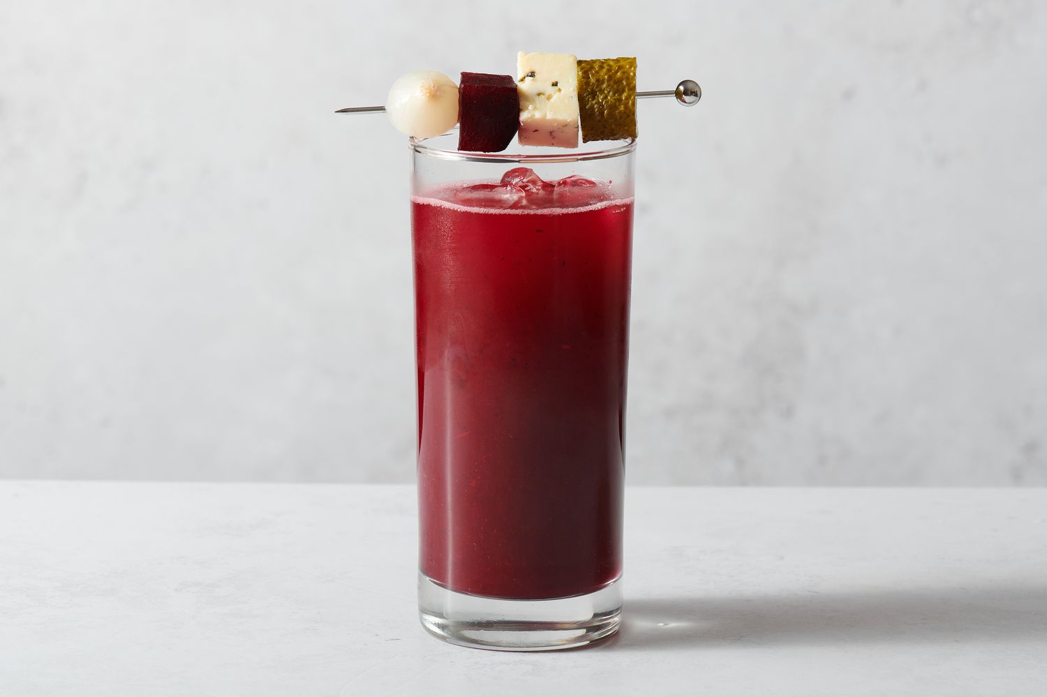 A Beet and Aquavit Bloody Mary garnished with roasted beets, cheese cubes, pickle slices, and pickled onions