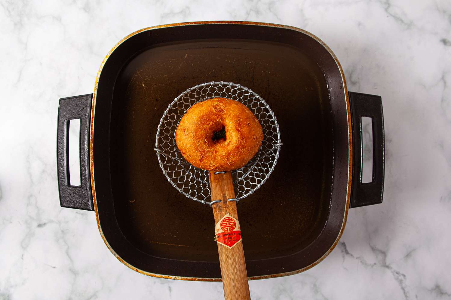 Fried doughnut draining over hot oil