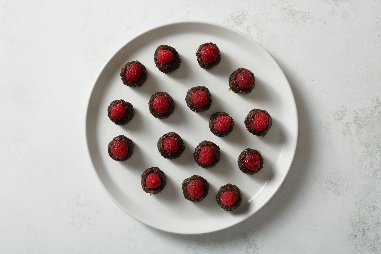 raspberries pushed inside of coconut balls on a plate