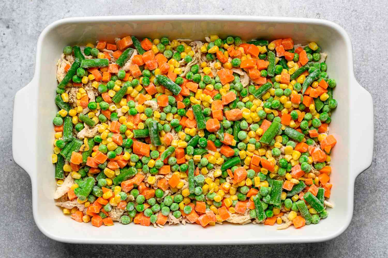 Salt, pepper, and frozen vegetables layered on top of the shredded chicken