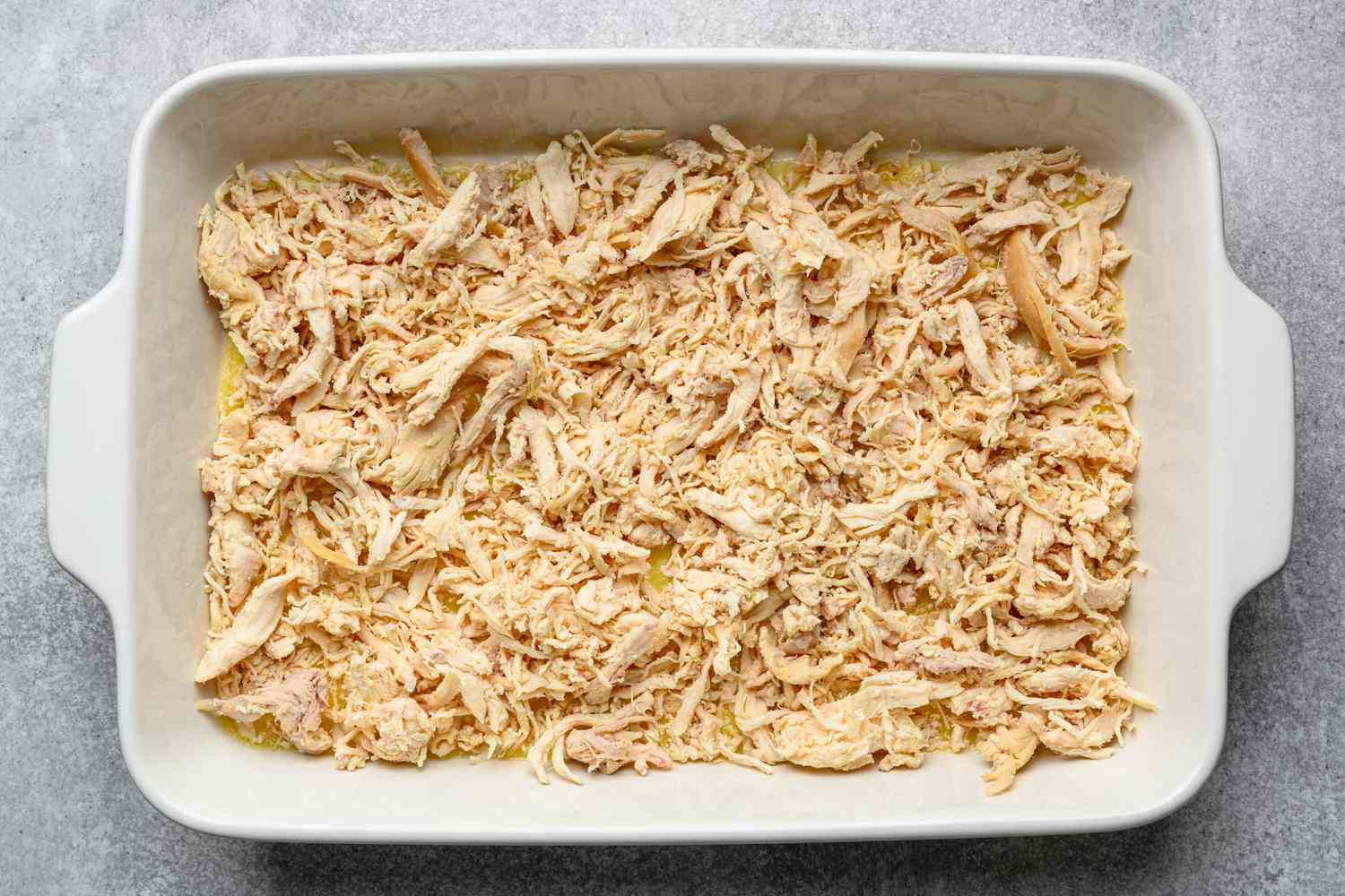 A 9 x 13 baking dish with melted butter and shredded chicken