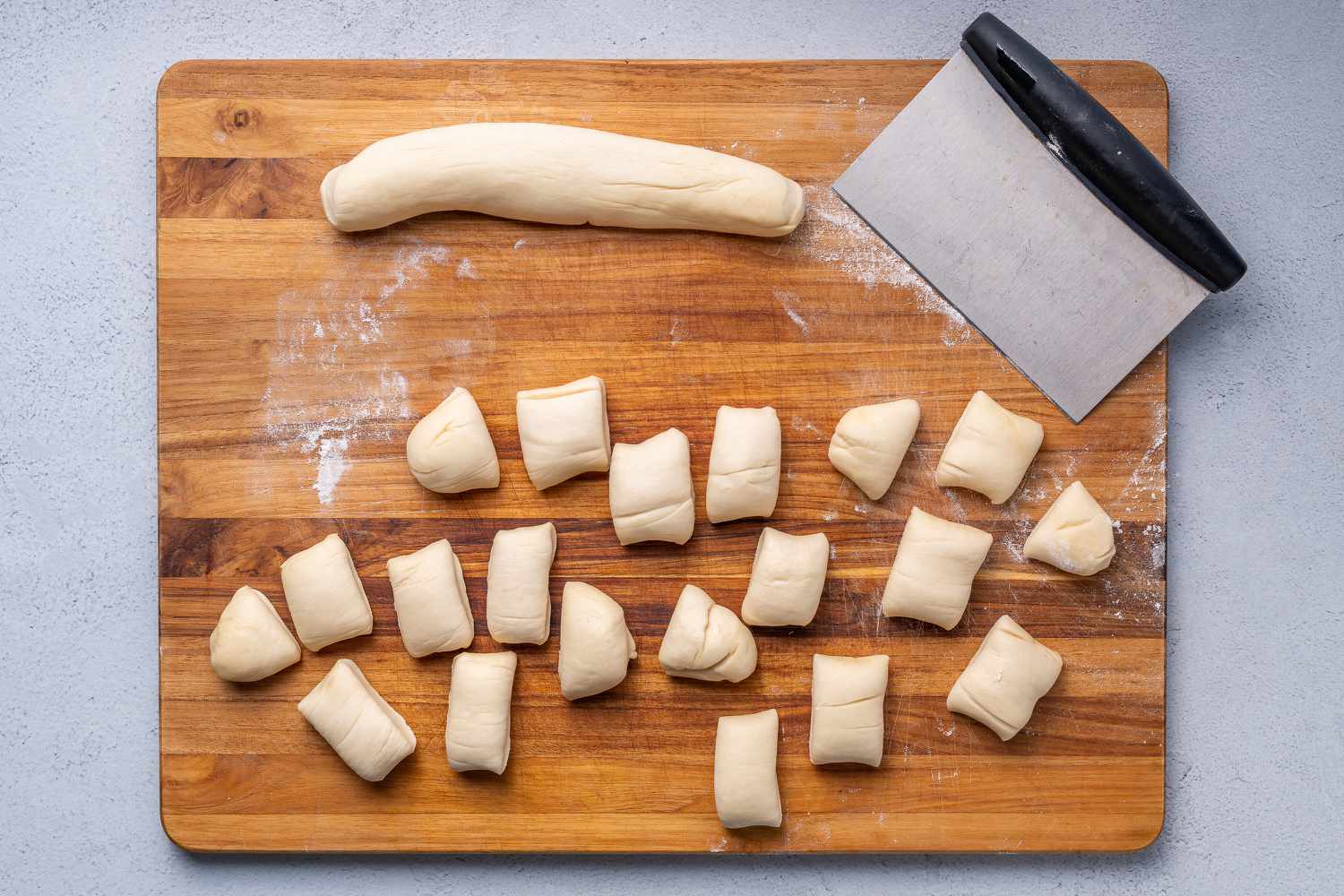 A roll of dough cut into 1 inch pieces on a cutting board