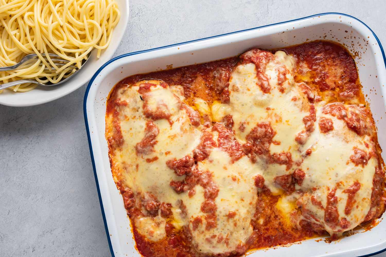 Easy Chicken Parmesan in a casserole dish next to a bowl of spaghetti