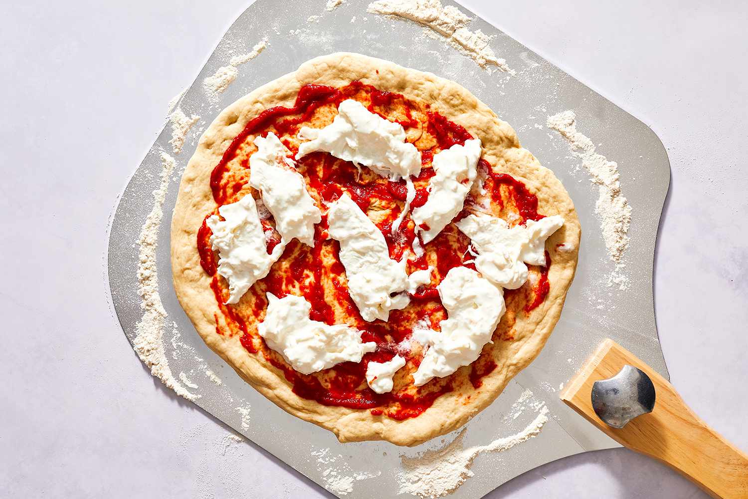 Pizza dough with tomato sauce and burrata cheese on a pizza peel