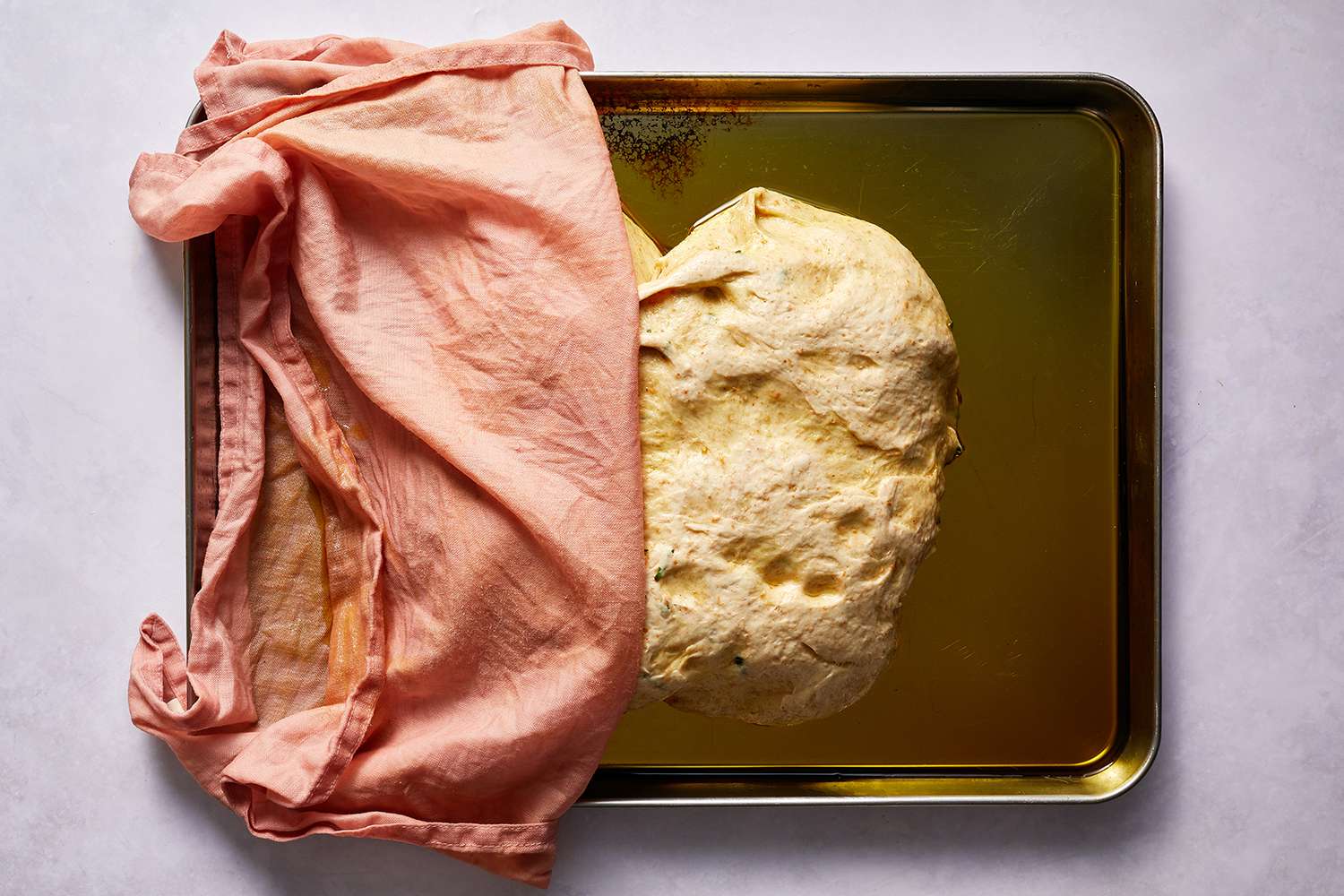 Rosemary focaccia dough on a baking sheet, covered with a towel 
