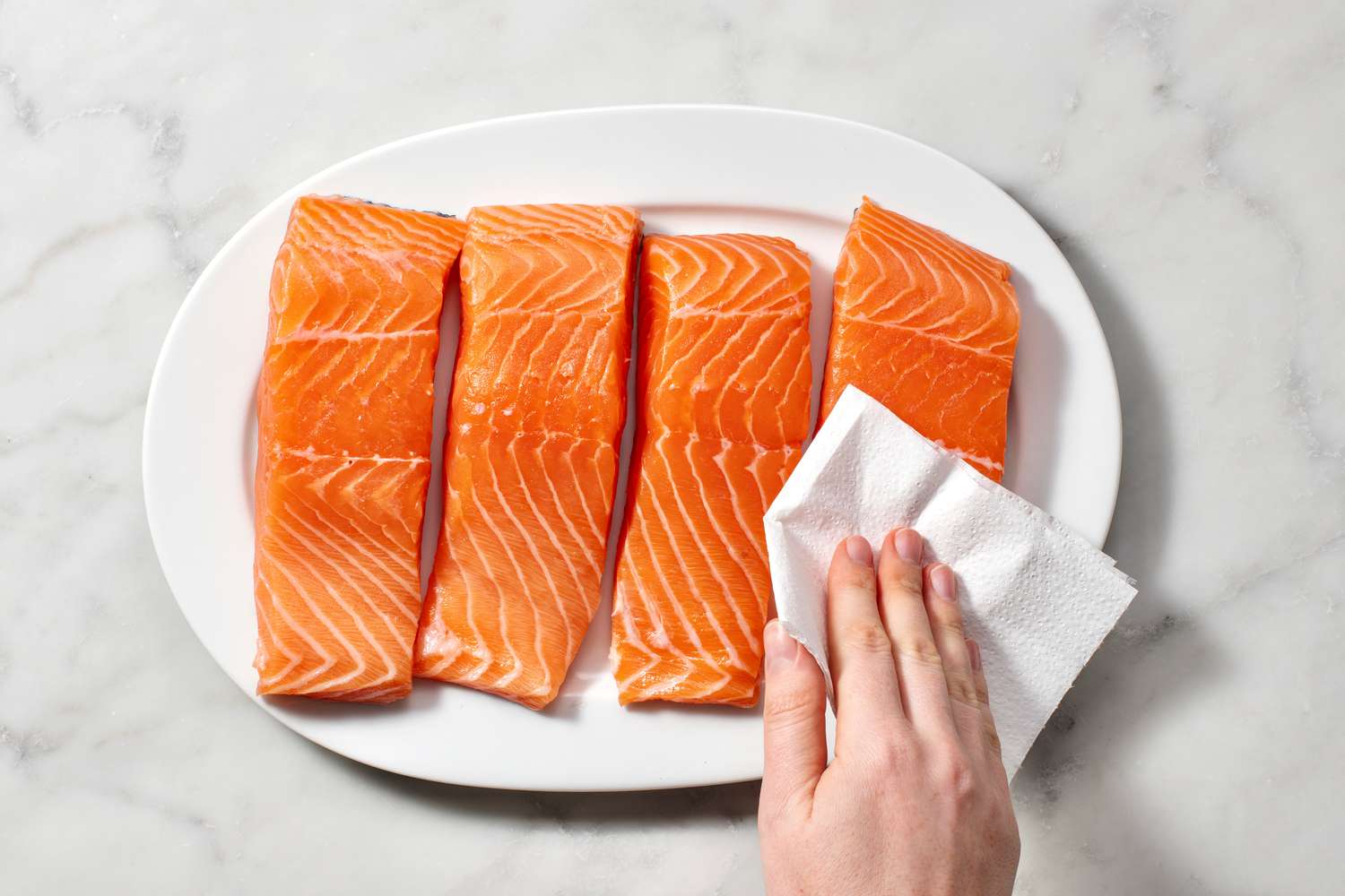 A hand patting salmon with a paper towel