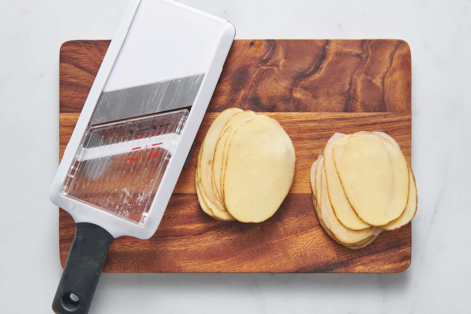 A cutting board and a mandolin with very thinly sliced potatoes
