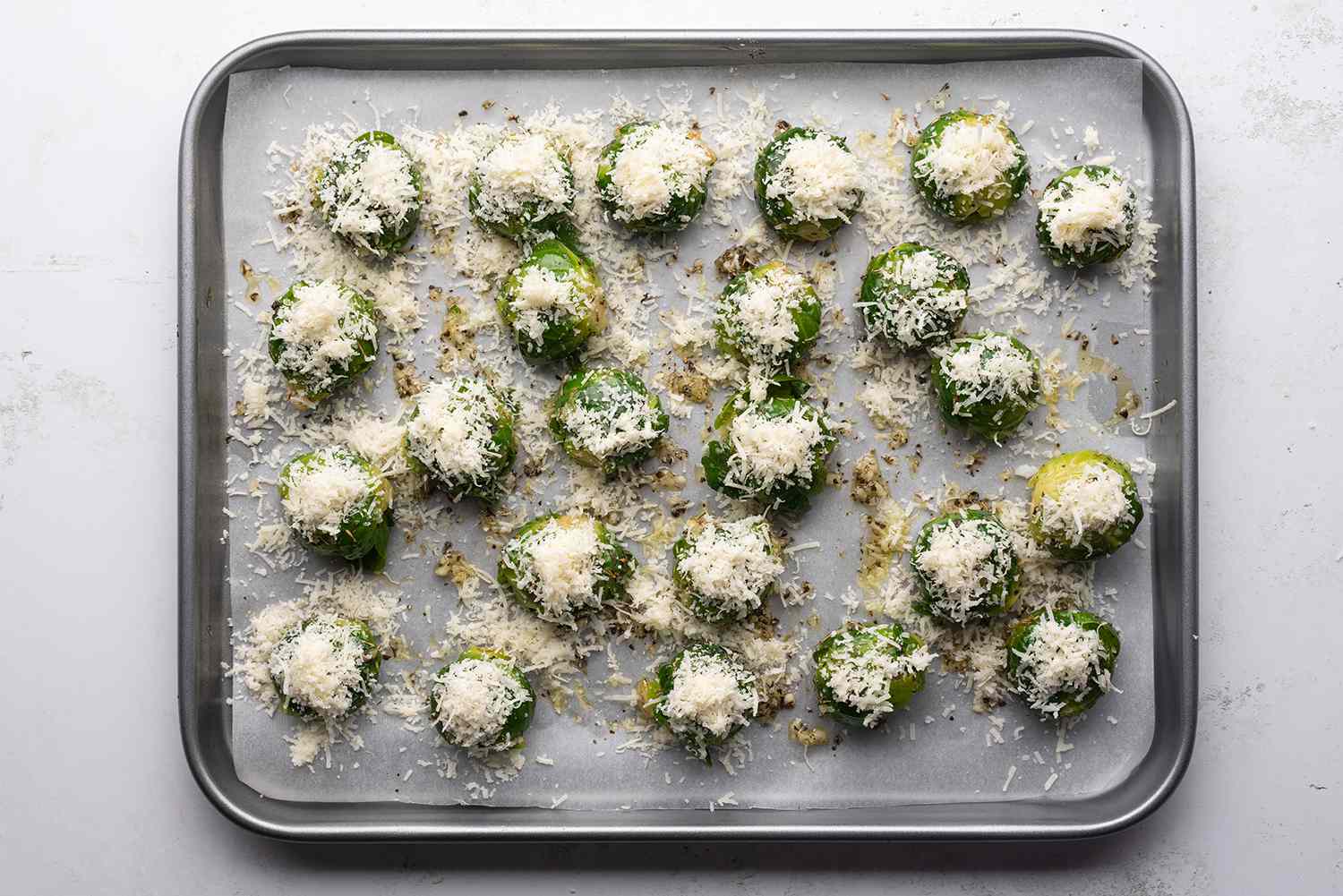 Brussels sprouts topped with parmesan cheese on a parchment paper lined baking sheet 