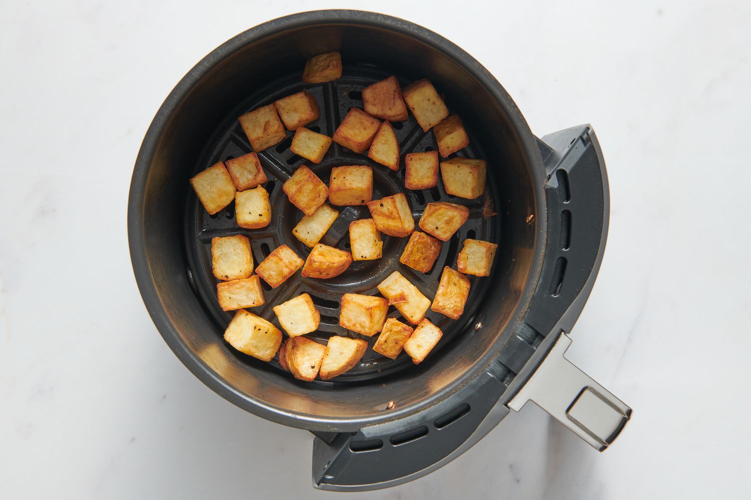 An air fryer basked with browned potato chunks