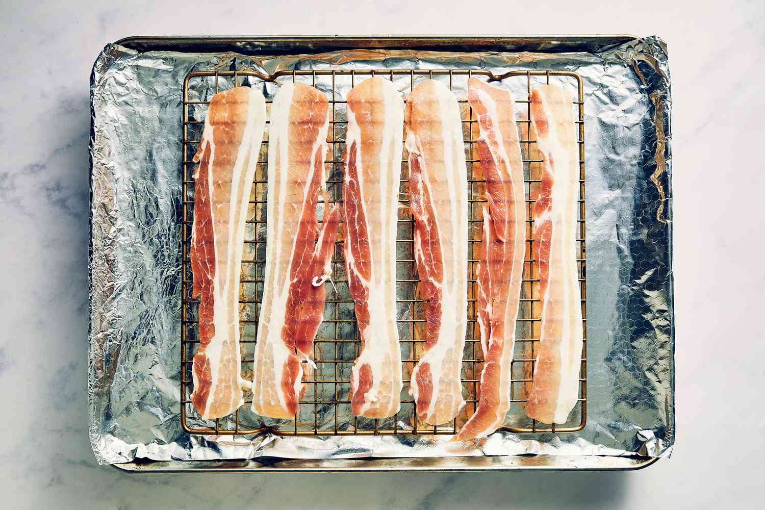 A sheet pan lined with foil with a baking rack, with thick pieces of thick cut bacon on the baking rack