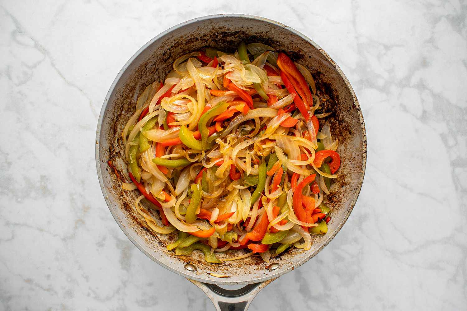 Sliced peppers and onions being sauteed in a large skillet