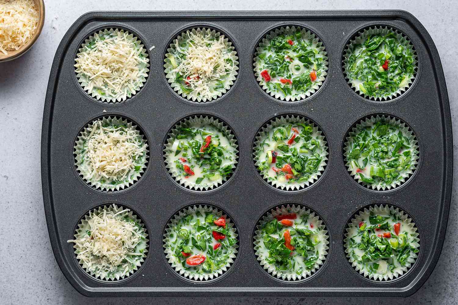 A muffin pan with egg mixture added, topped with parmesan cheese