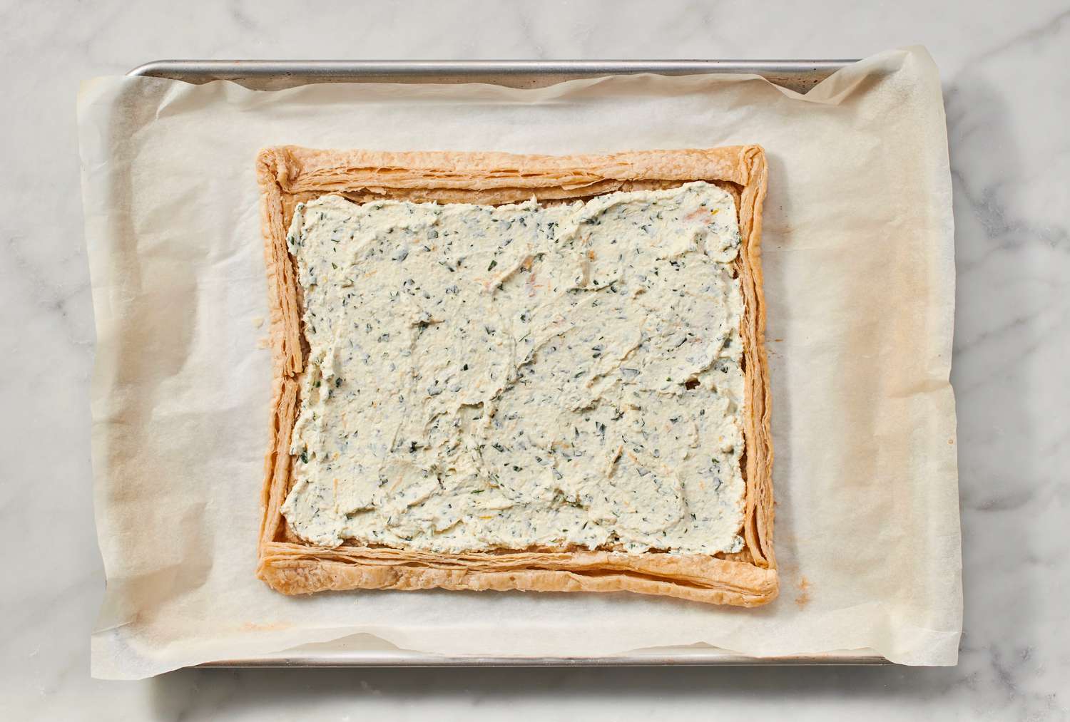 A partially baked puff pastry crust covered in the seasoned cream cheese mixture