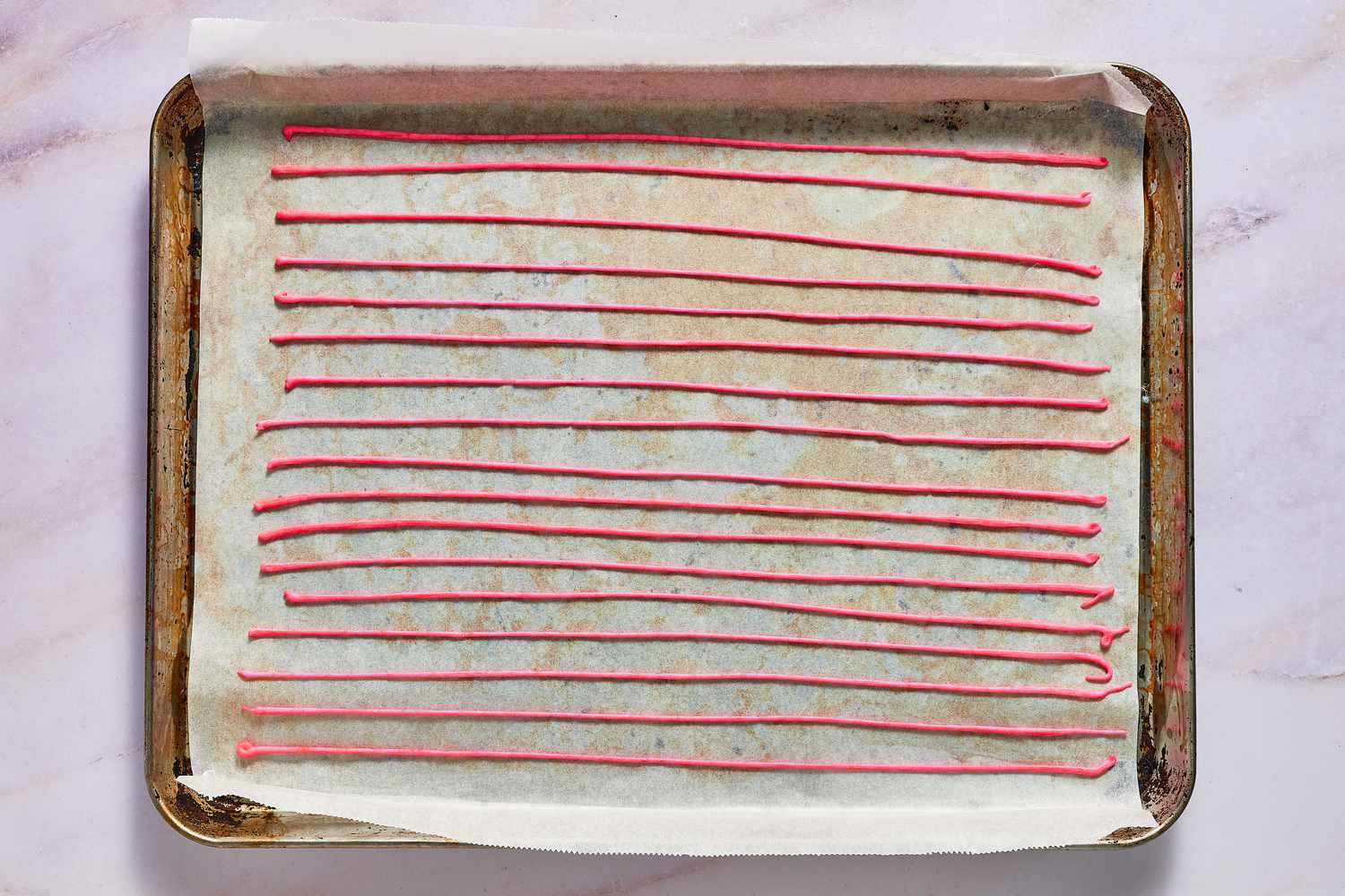 A parchment paper-lined baking sheet with long lines of red sprinkles