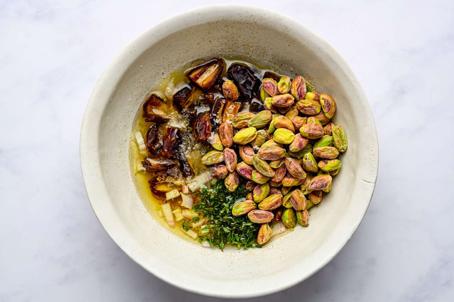 A bowl with olive oil, honey, thyme, dates, nuts, salt, and pepper