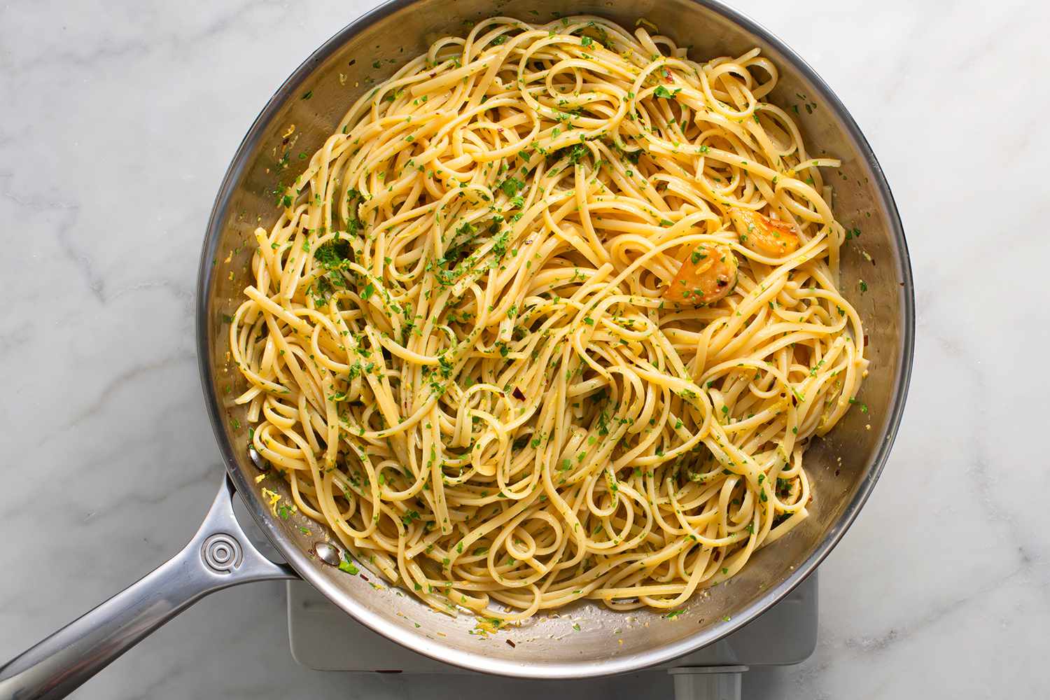 Parsley, the lemon zest, and juice added to the pasta in the pan, on a burner 