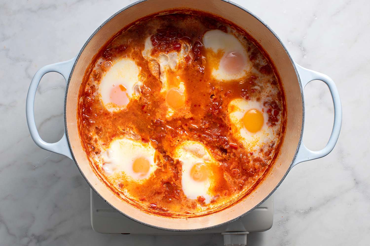 Eggs cooking in the tomato sauce in a pot on a burner 