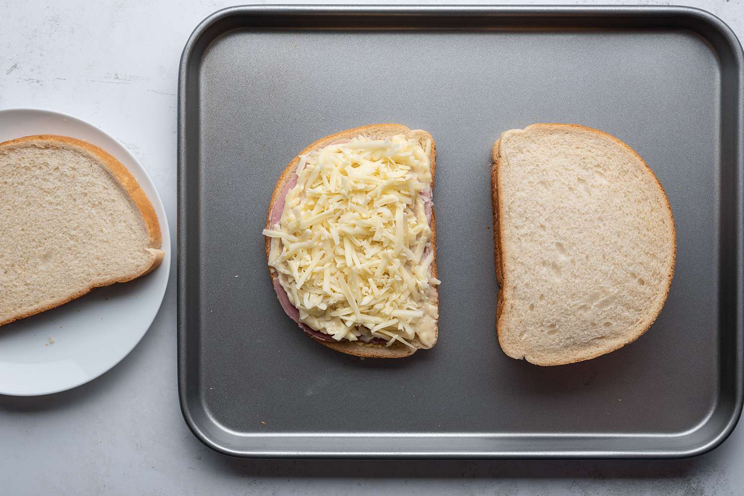 Cheese, bread and ham sandwiches on a sheet pan, and bread on a plate 