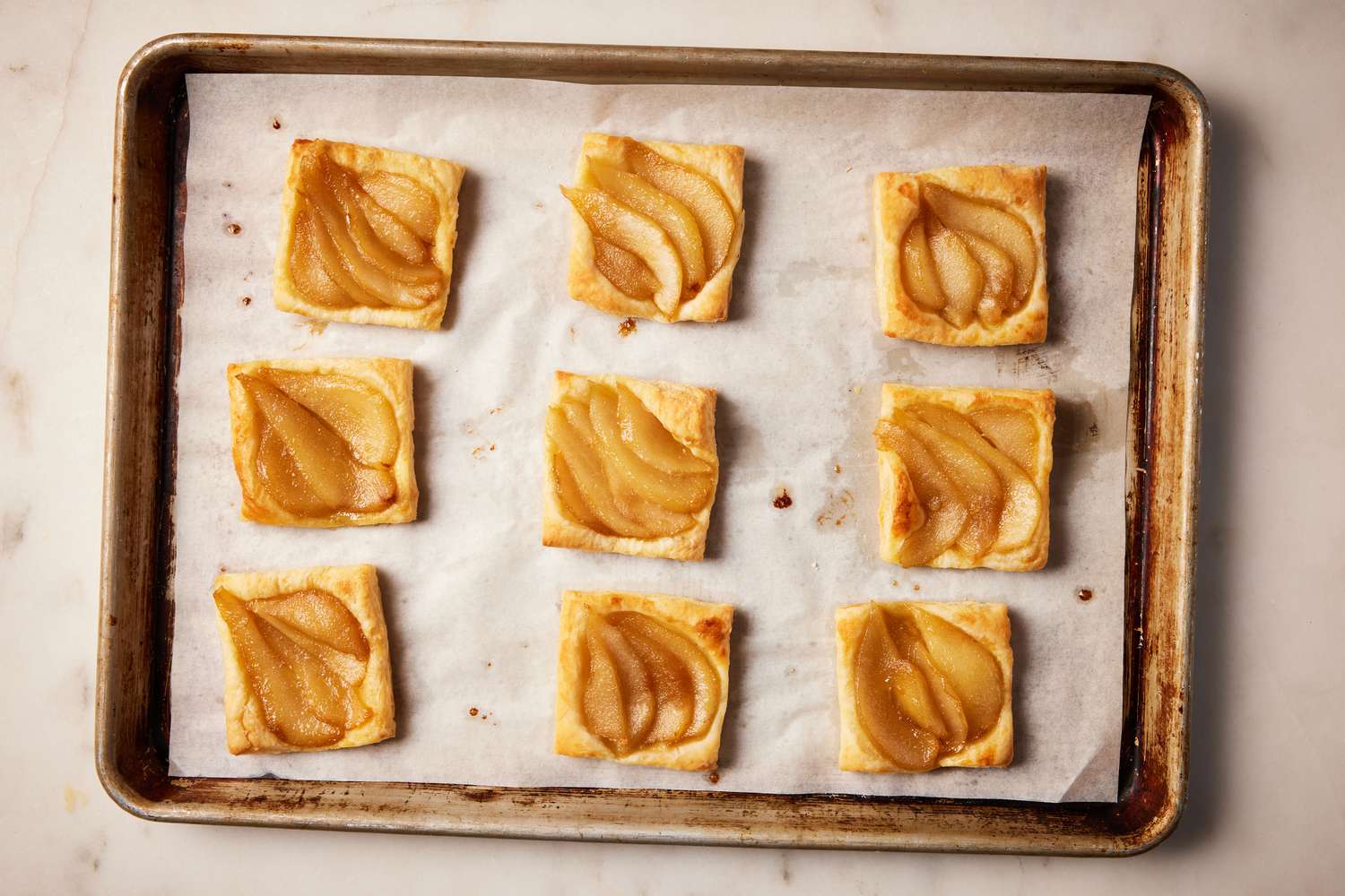 A parchment paper-lined baking sheet with nine baked individual pear tarts
