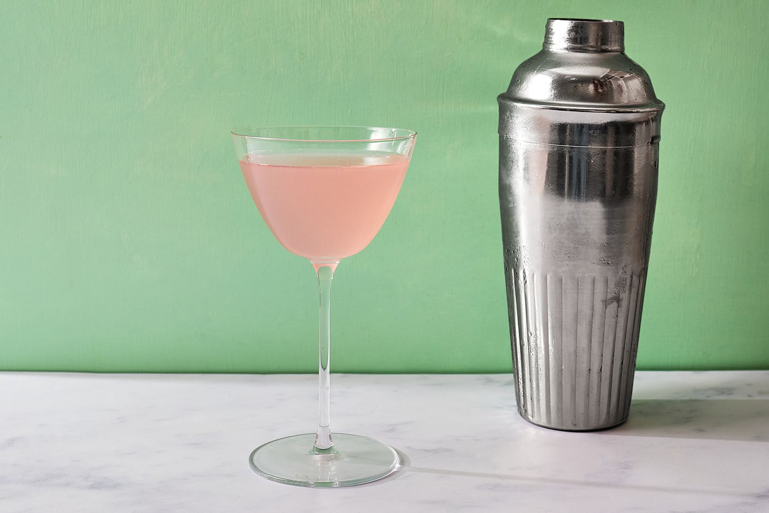 Cosmopolitan Cocktail in a glass, next to a cocktail shaker 
