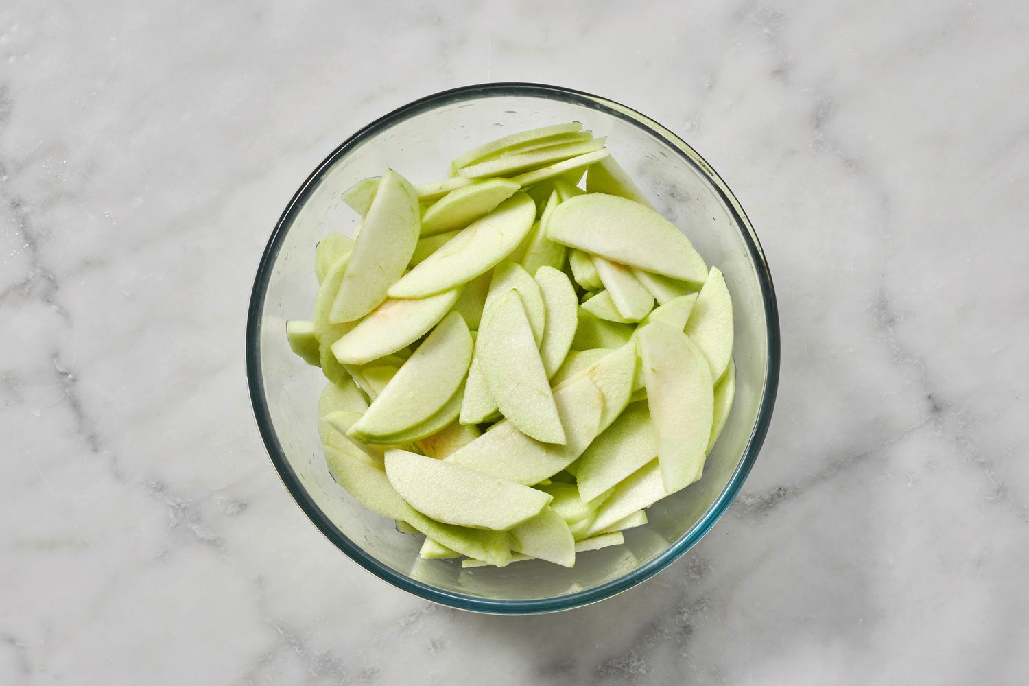 A bowl of thinly sliced apples in a glass bowl, tossed with lemon juice
