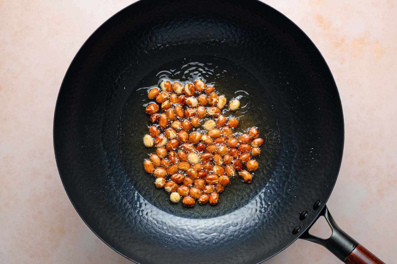 A large wok with peanuts cooking in oil