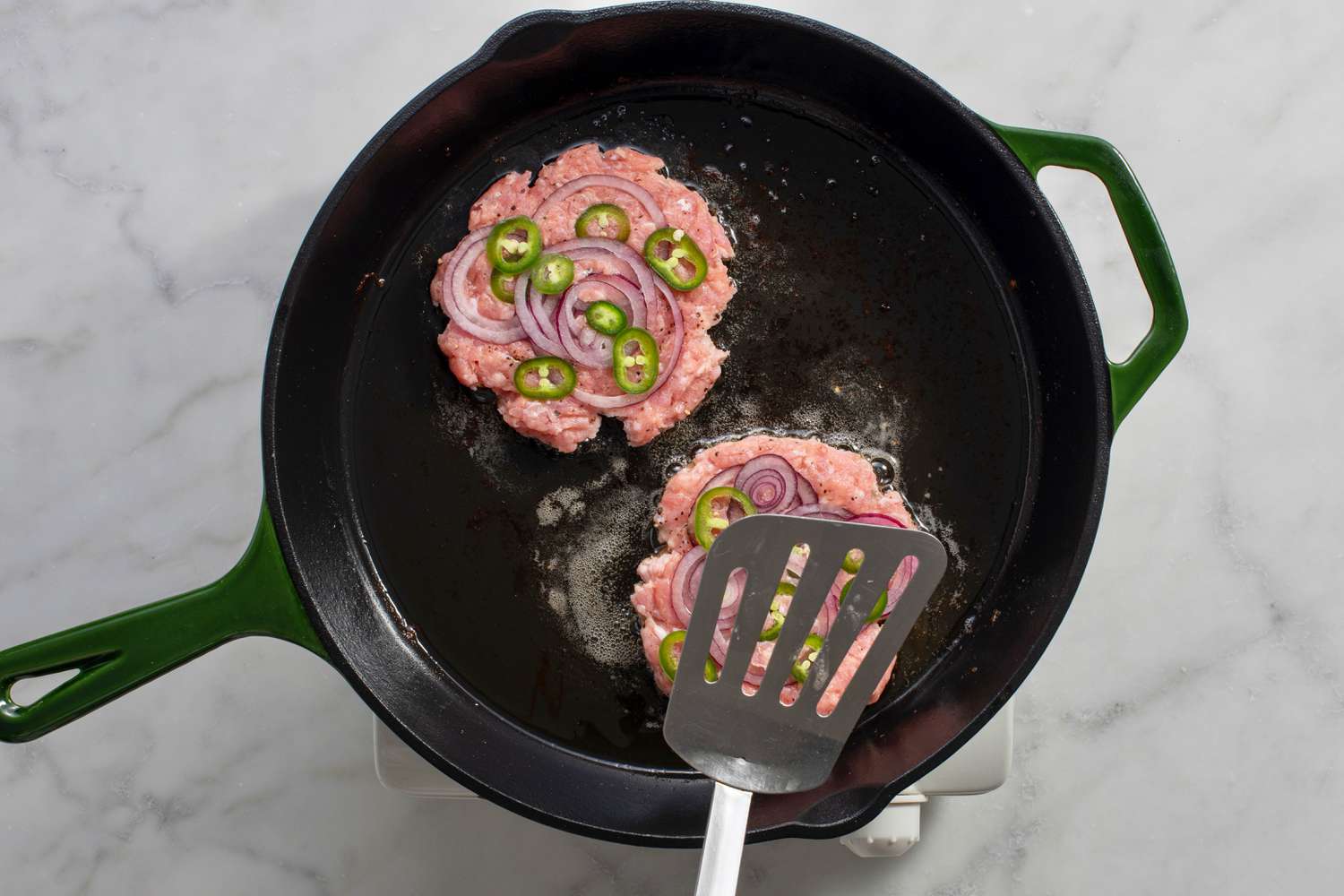 Chicken patties topped with onions and jalapenos being flattened by a spatula
