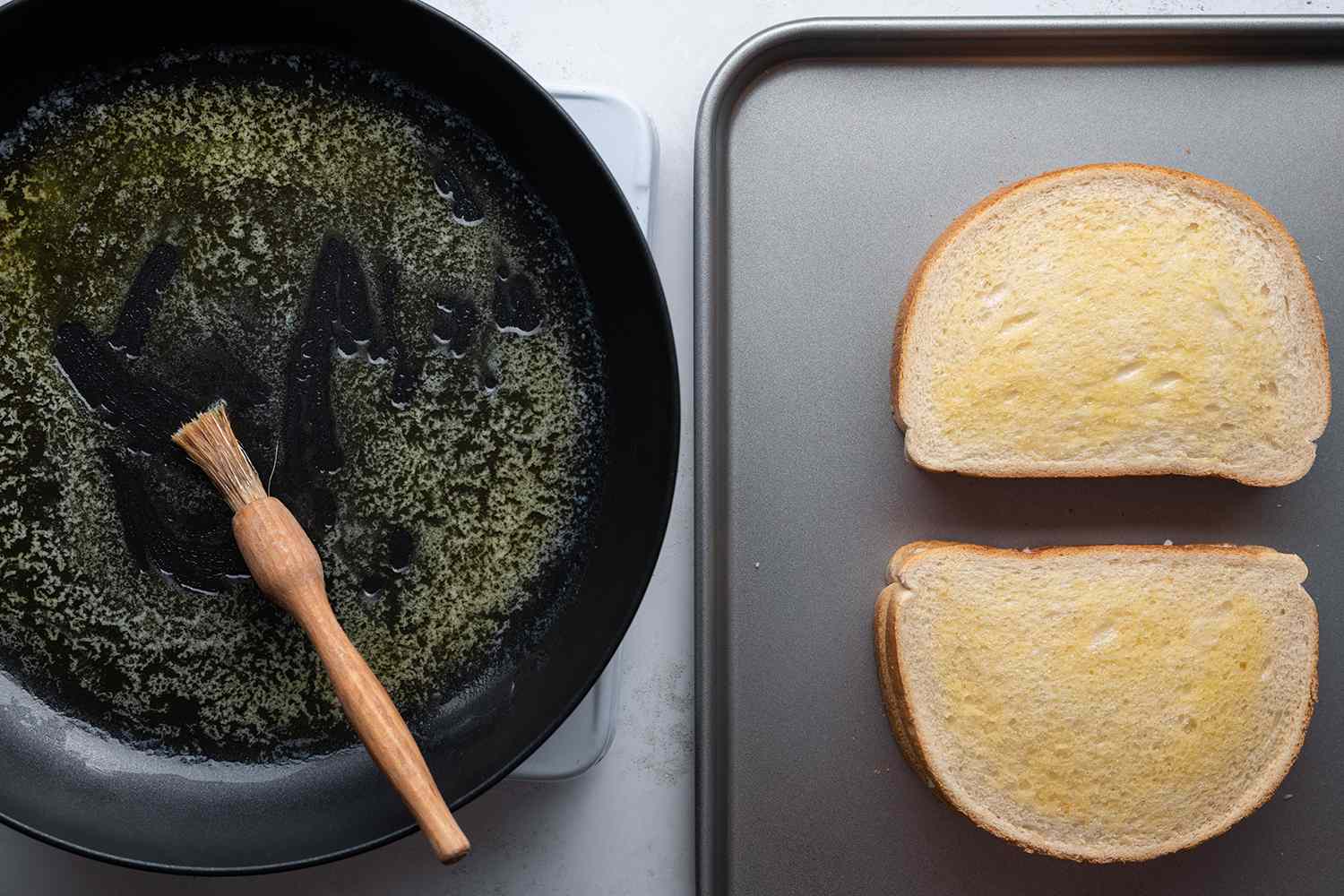 Butter in a pan with a brush on a burner, and sandwiches on a sheet pan 
