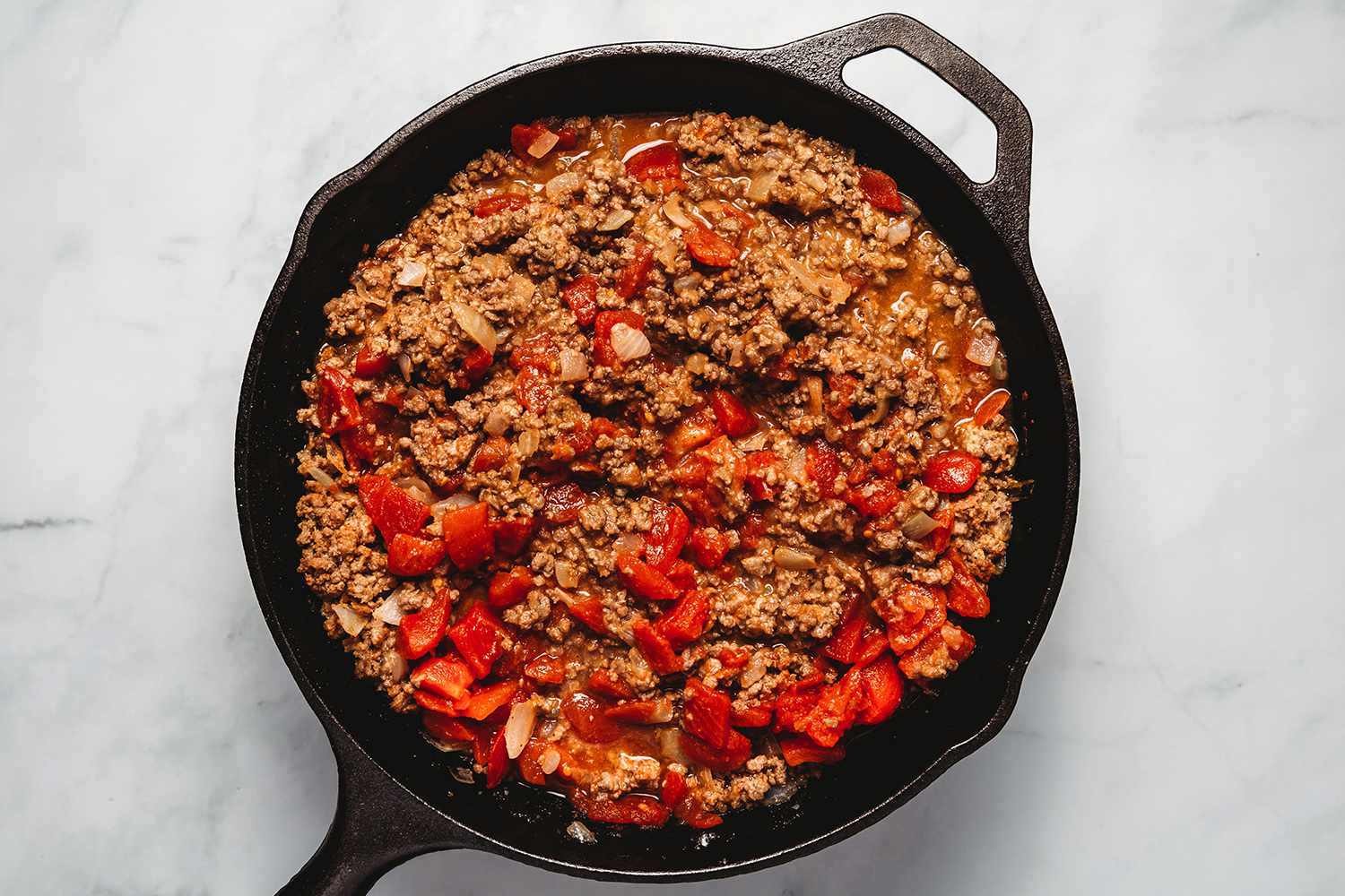 Worcestershire, beef broth, and tomatoes added to the beef mixture in a cast iron skillet 