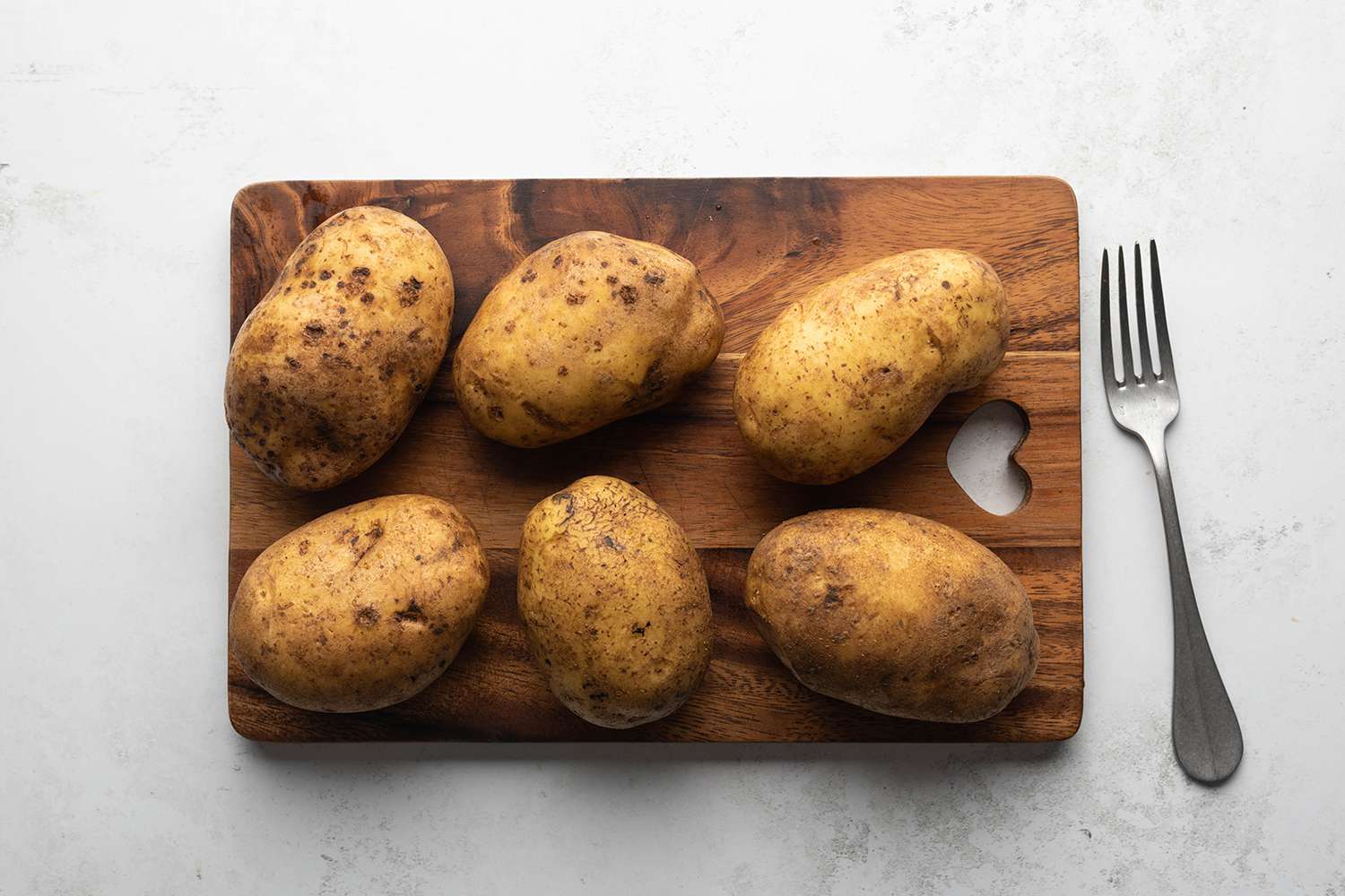 Potatoes on a wooden cutting board, next to a fork 