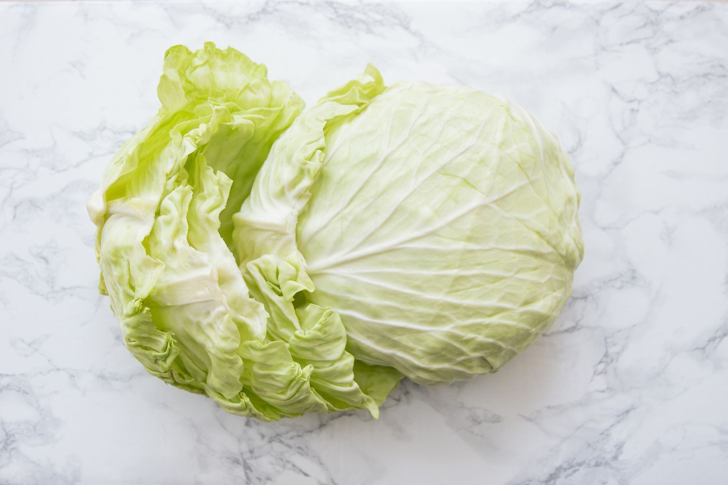Cabbage head with leaves removed on a white marble table