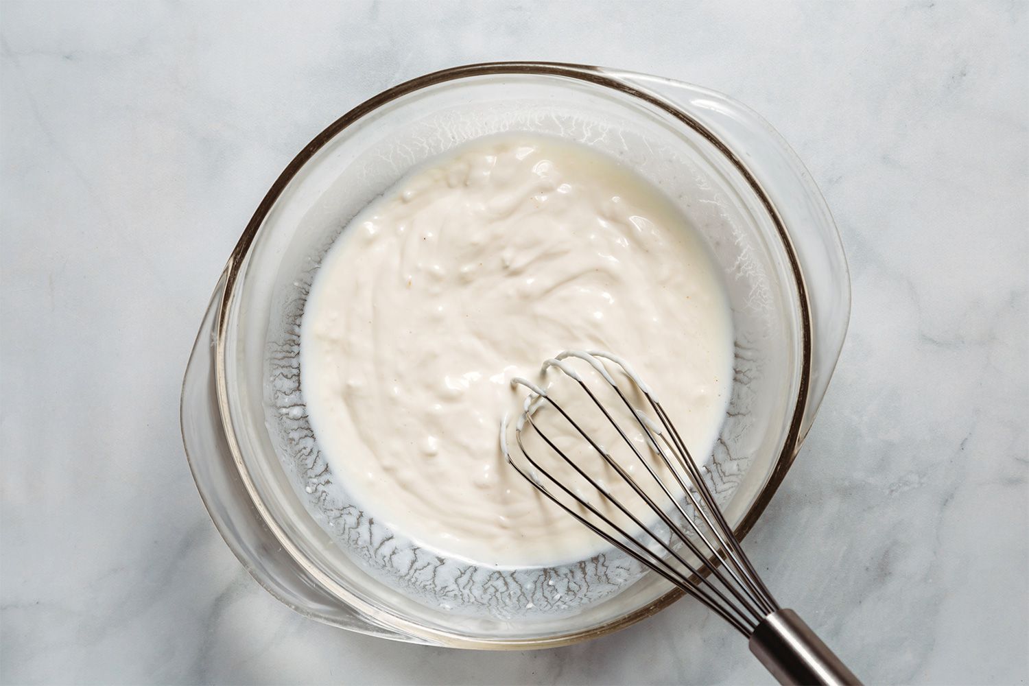 Buttermilk, mayonnaise, and sour cream in a bowl with a whisk 