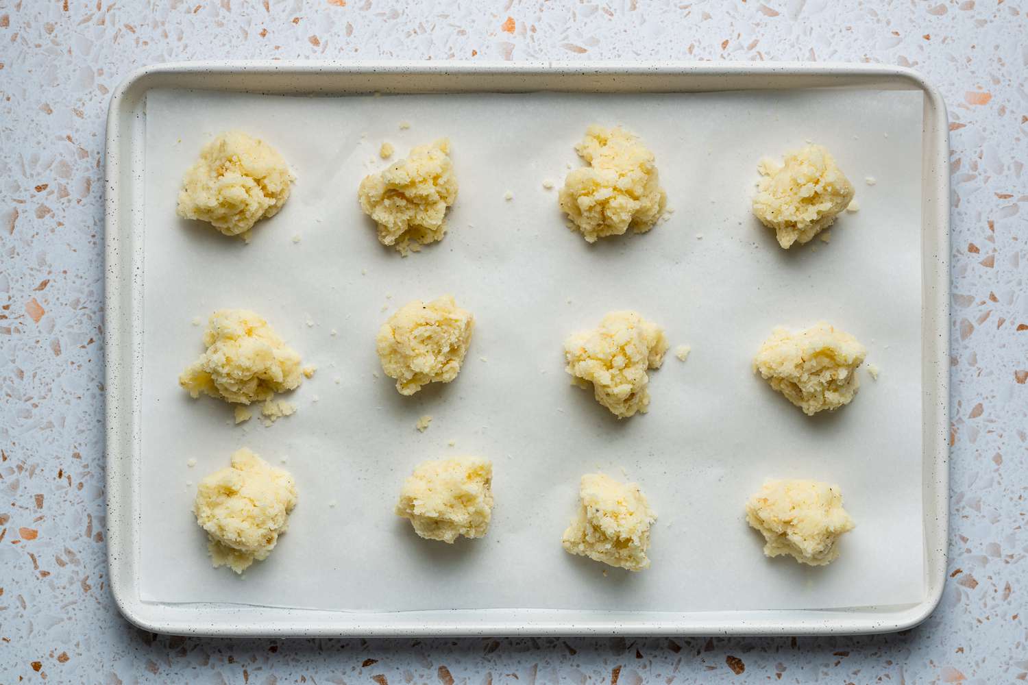 A parchment paper-lined baking sheet with 12 equal portions of the coconut laddoo mixture