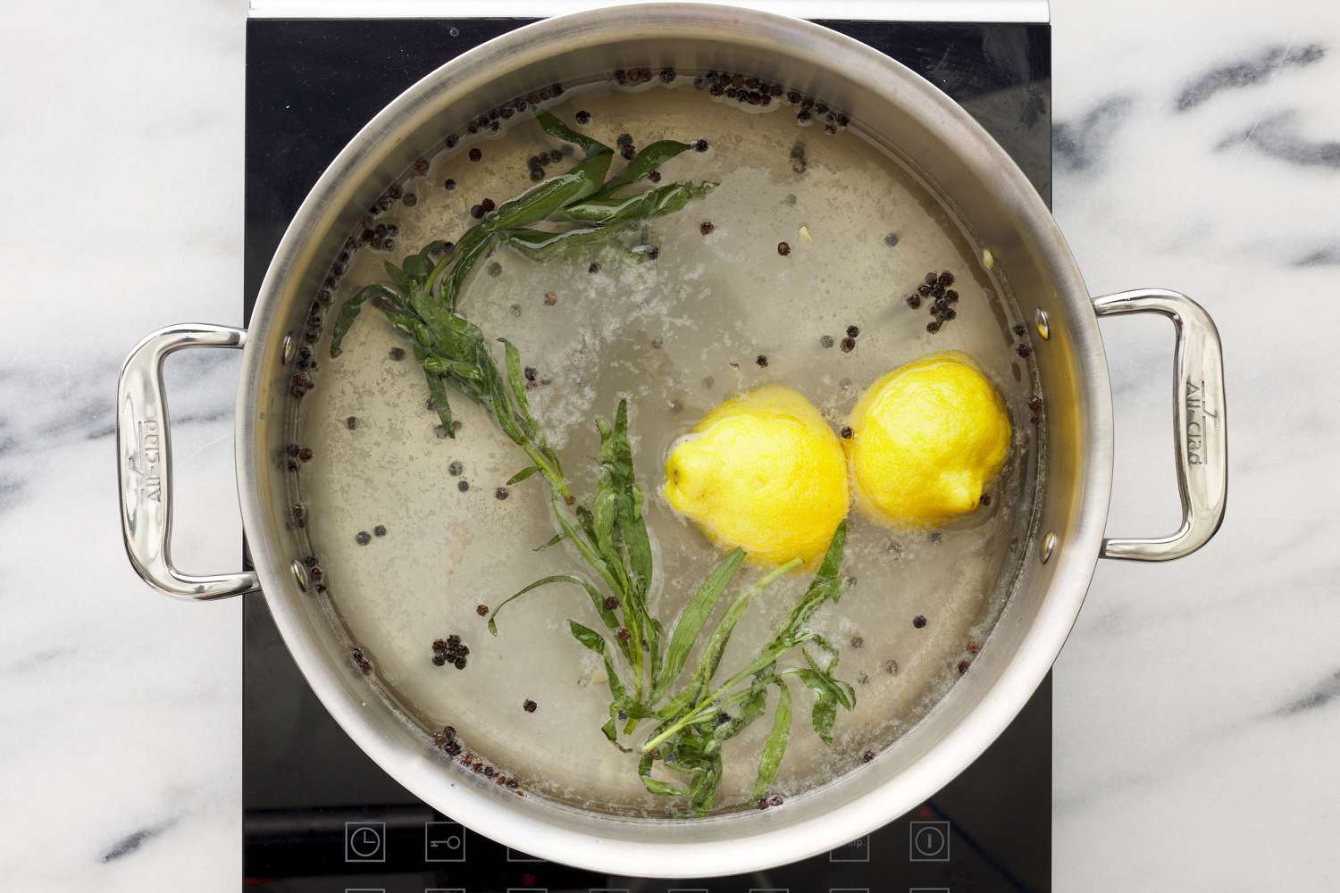 A large pot with water, salt, sugar, whole peppercorns, tarragon sprigs, and a halved lemon