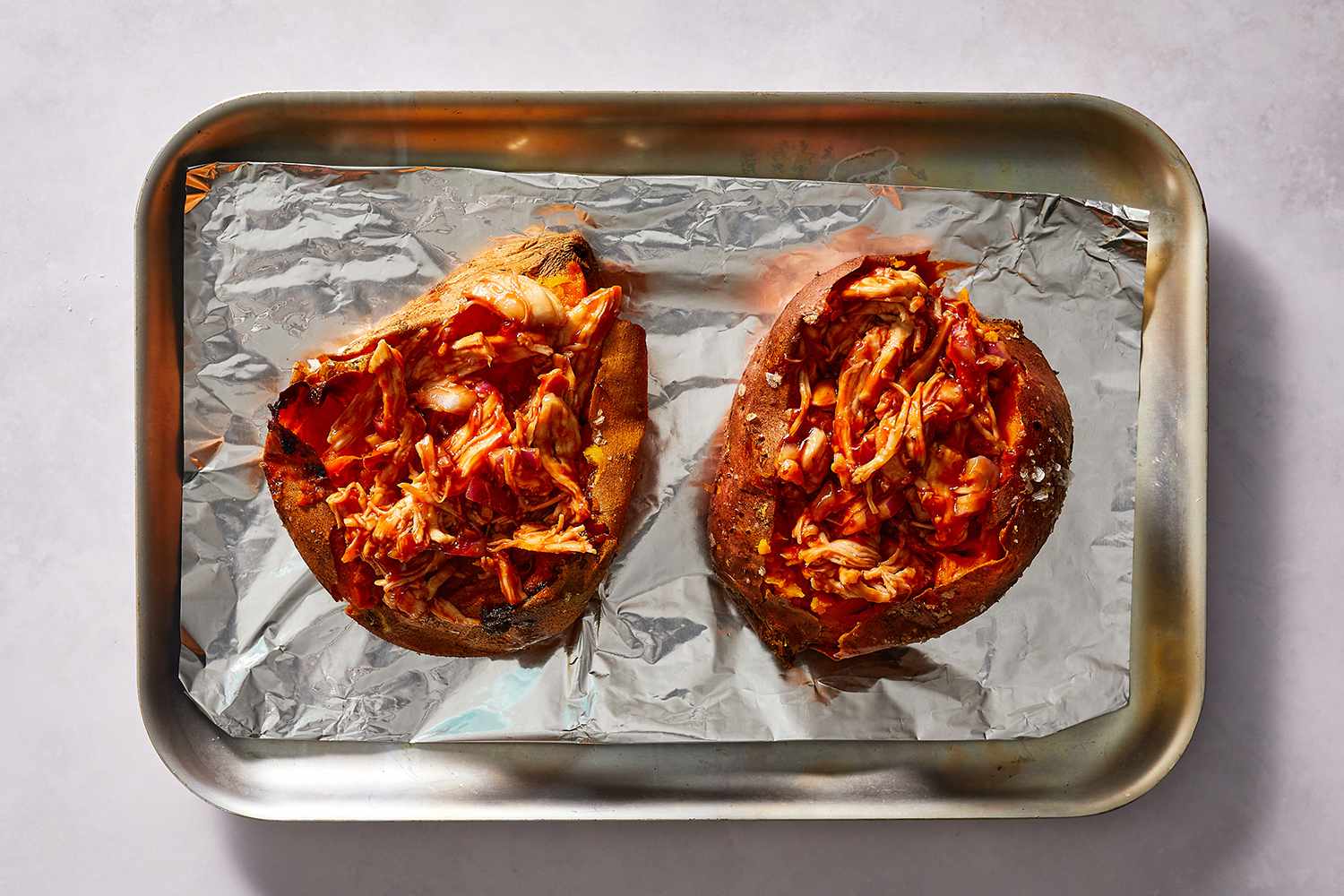 Sweet potatoes topped with barbecue chicken on a baking sheet 
