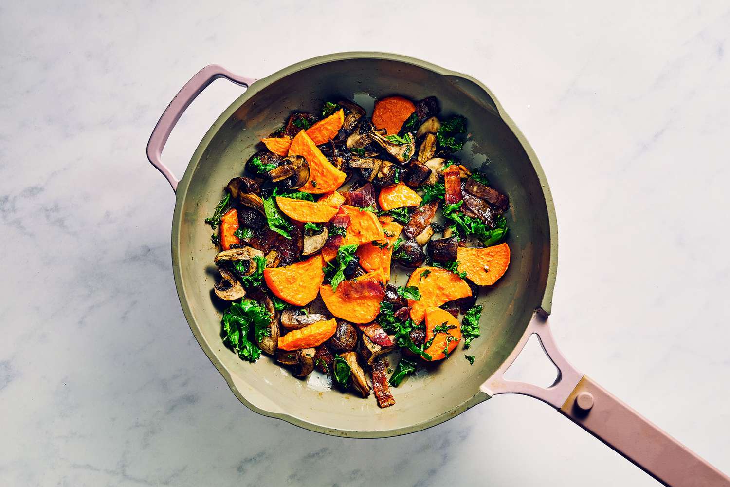 A small skillet with roasted mushrooms, roasted sweet potatoes, chopped kale, and million dollar bacon pieces