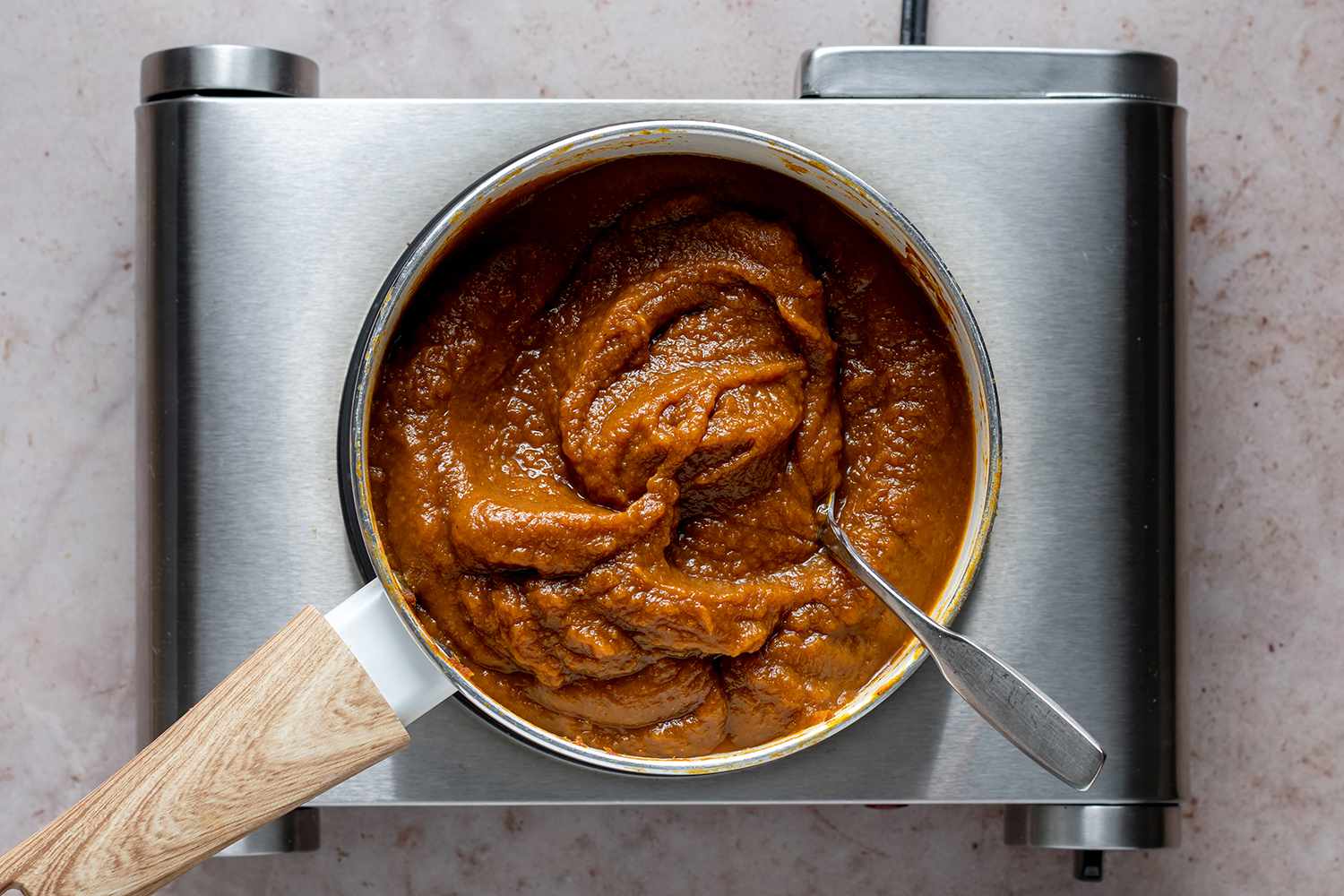 Pumpkin Butter in a pan on a burner, with a metal spoon 