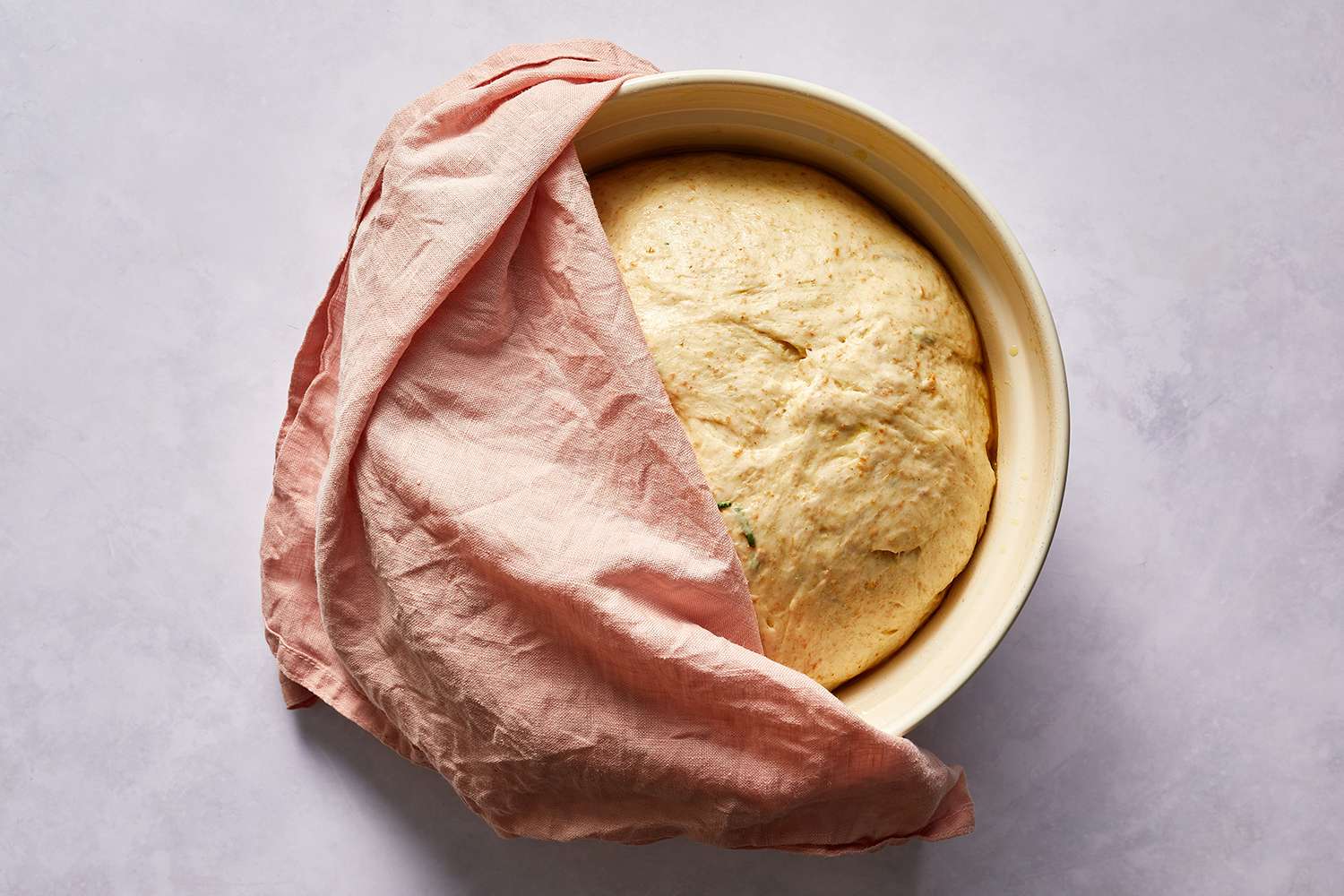 Rosemary focaccia dough in a bowl, covered with a towel 