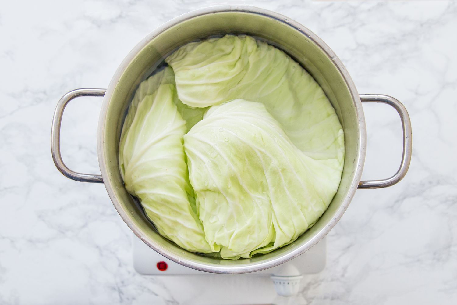 Cabbage leaves in a pot of salted water, on a white marble table