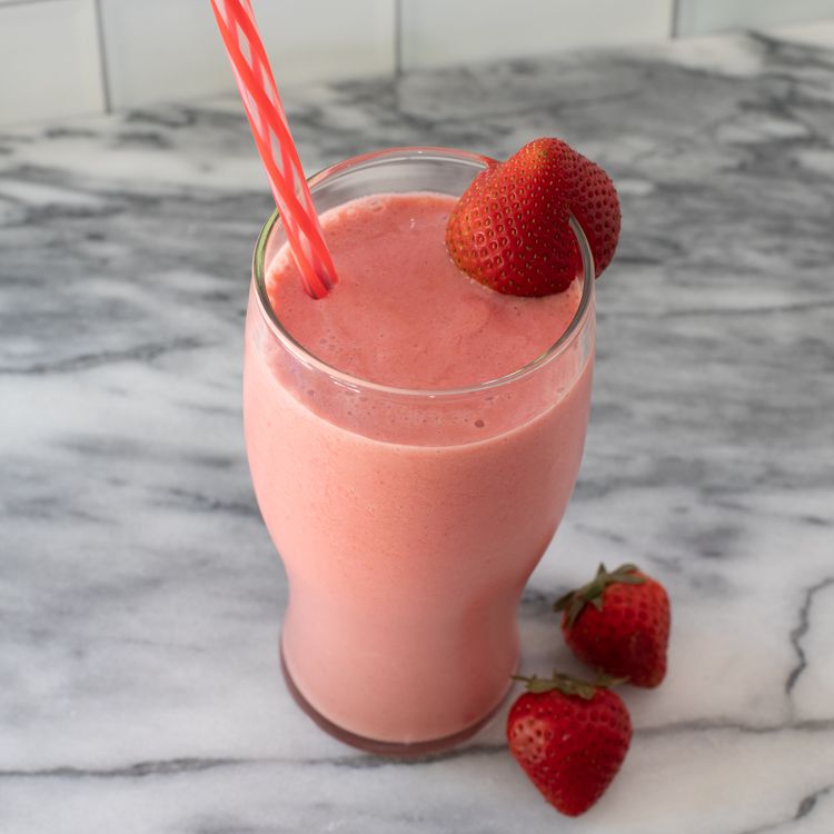 Strawberry smoothie in a glass with a straw and strawberry garnish
