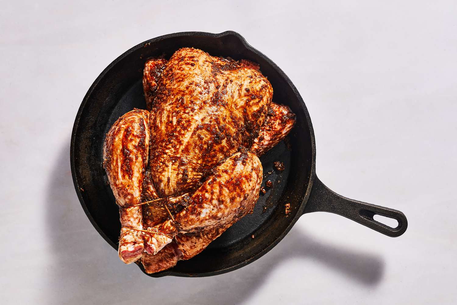 A trussed, whole chicken in a cast iron skillet coasted in the spice-oil mixture