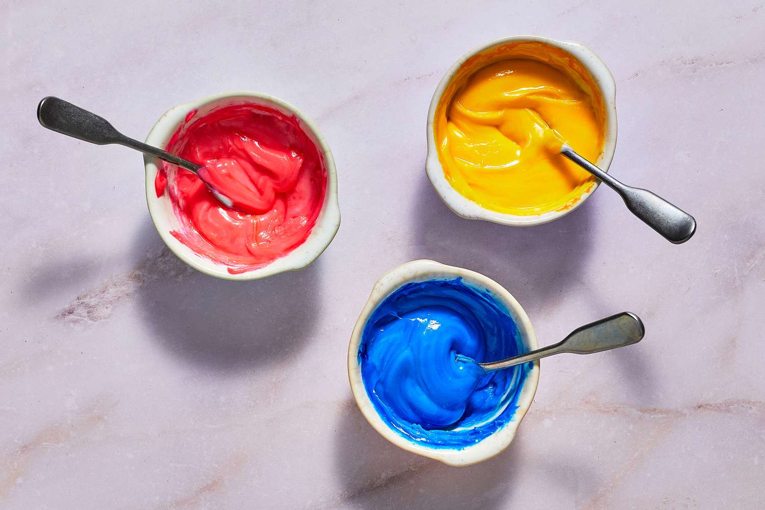 Small bowls of red, yellow, and blue sprinkle batter