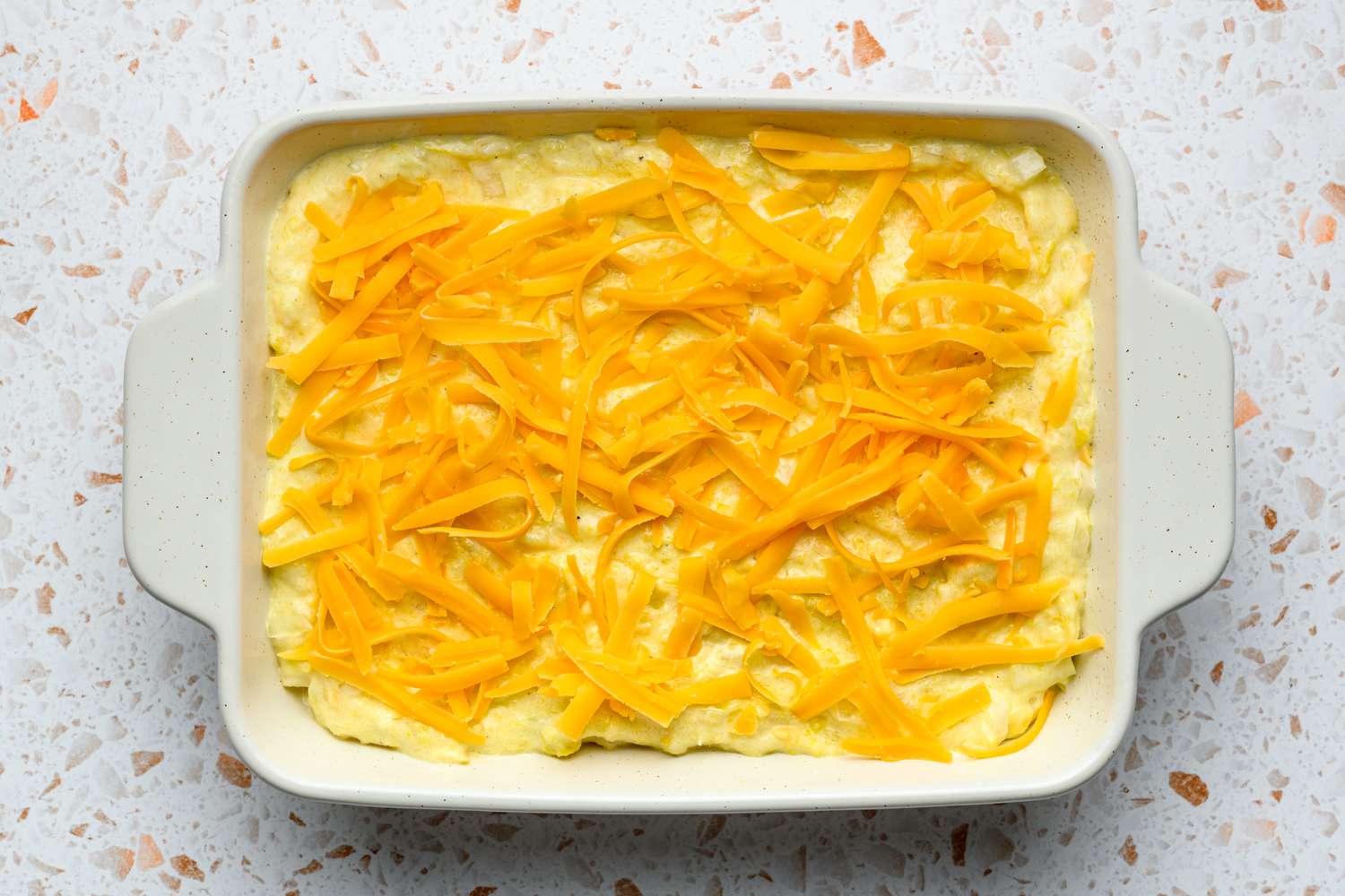 A baking dish with unbaked mashed yellow squash mixture topped with shredded cheese
