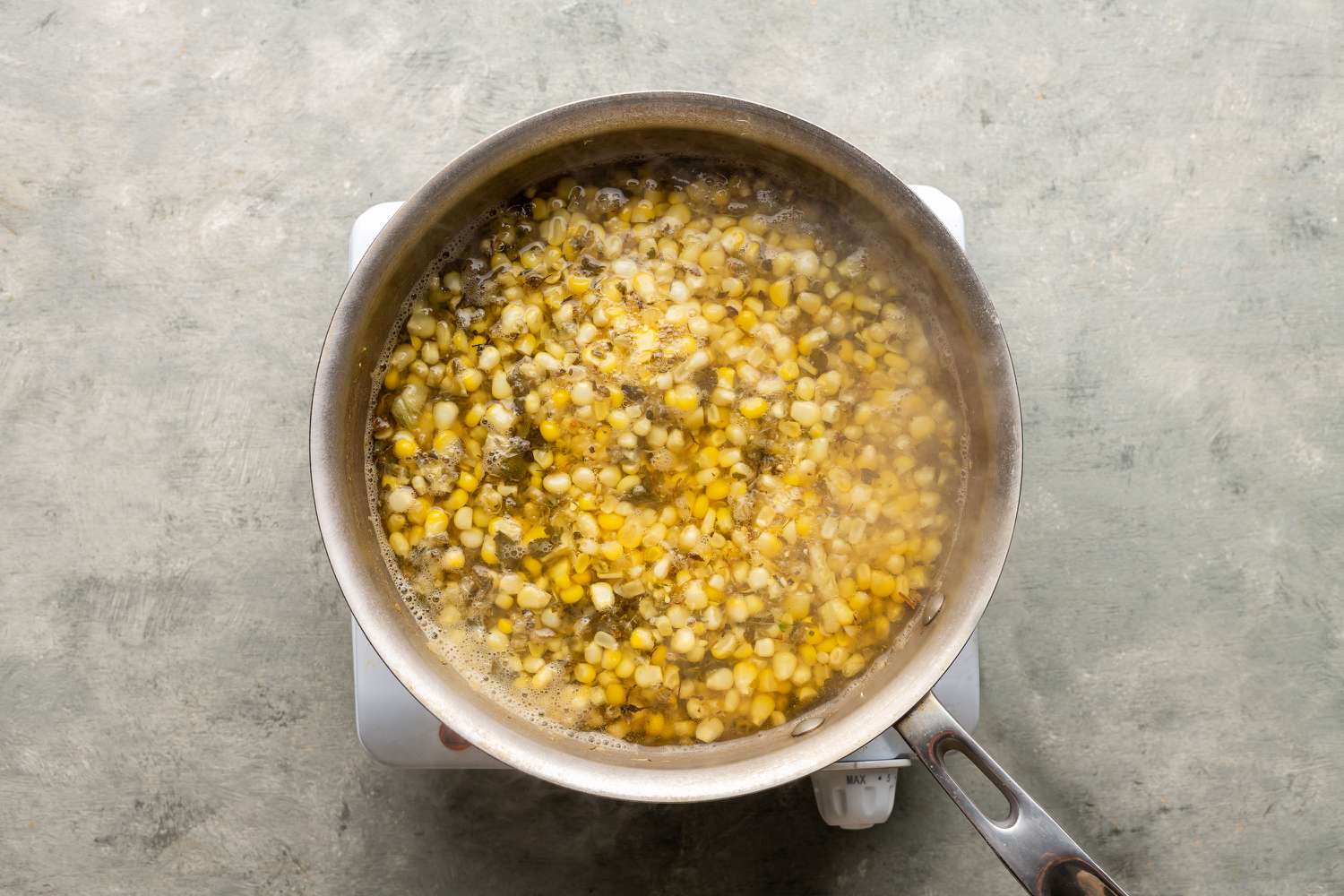 Corn, water, epazote leaves, and salt in a pot on the burner 